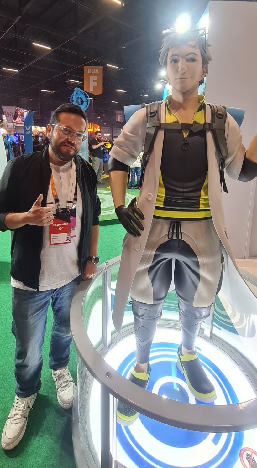 A man in glasses stands next to a large statue of an anime-style character dressed like an eccentric scientist.