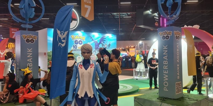 An image of a booth in a convention centre with an anime-style statue at center, others at the sides and fans milling around.