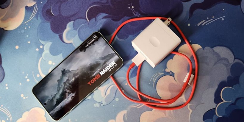 OnePlus 15R with Tomb Raider on screen sitting next to the orange charging cord
