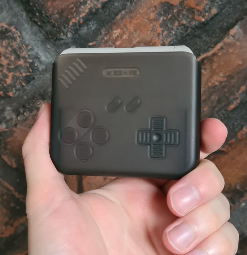A picture of a device in a gray case, with engravings mimicking the style of an old game controller, background is brick.