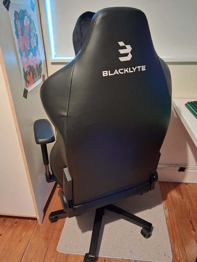 The back of a gaming chair, facing towards the wall, it is large and sandwiched between a cupboard and a desk which is just out of shot.